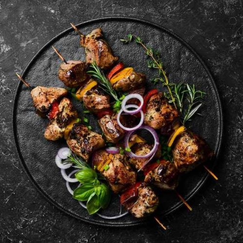 traditional-kebab-juicy-pork-skewers-with-vegetables-black-stone-plate-barbecue-top-view-free-space-text_187166-44336